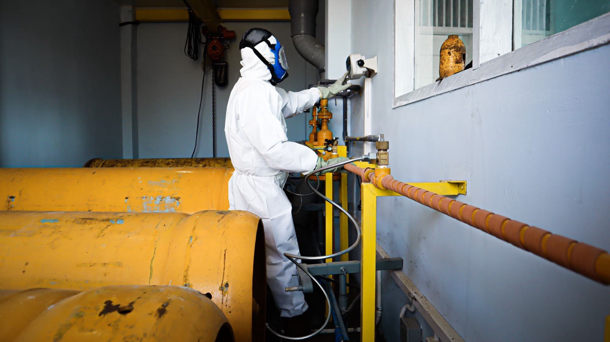 A technician in full protective equipment operating cylinder filling equipment at a Suez Gas plant